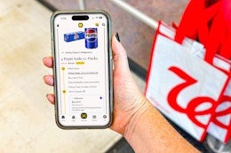 hand holding smartphone with kcl app 1-clip coupons next to a walgreens shopping bag