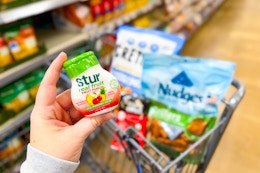 hand holding a bottle of stur in front of a blurred card with cretors, nudges, and oceans halo items