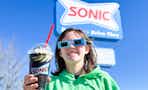a person holding out a sonic black out drink wearing the free eclipse glasses 
