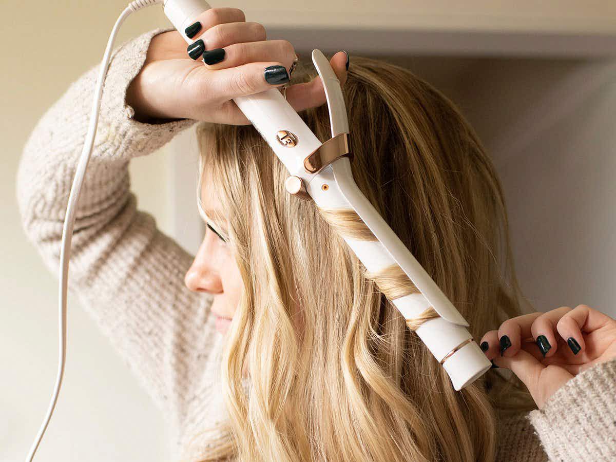 A woman using a T3 curling iron to curl her long blond hair.