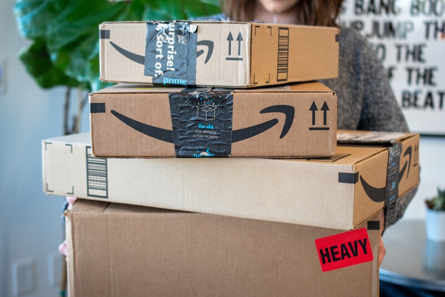 A woman holding a stack of 4 amazon delivery boxes.