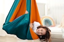 A young girl smiles while her body is hugged by a fabric sensory swing that hangs from the ceiling, Autism ASD Sensory