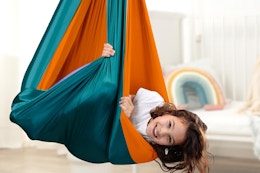 A young girl smiles while her body is hugged by a fabric sensory swing that hangs from the ceiling, Autism ASD Sensory