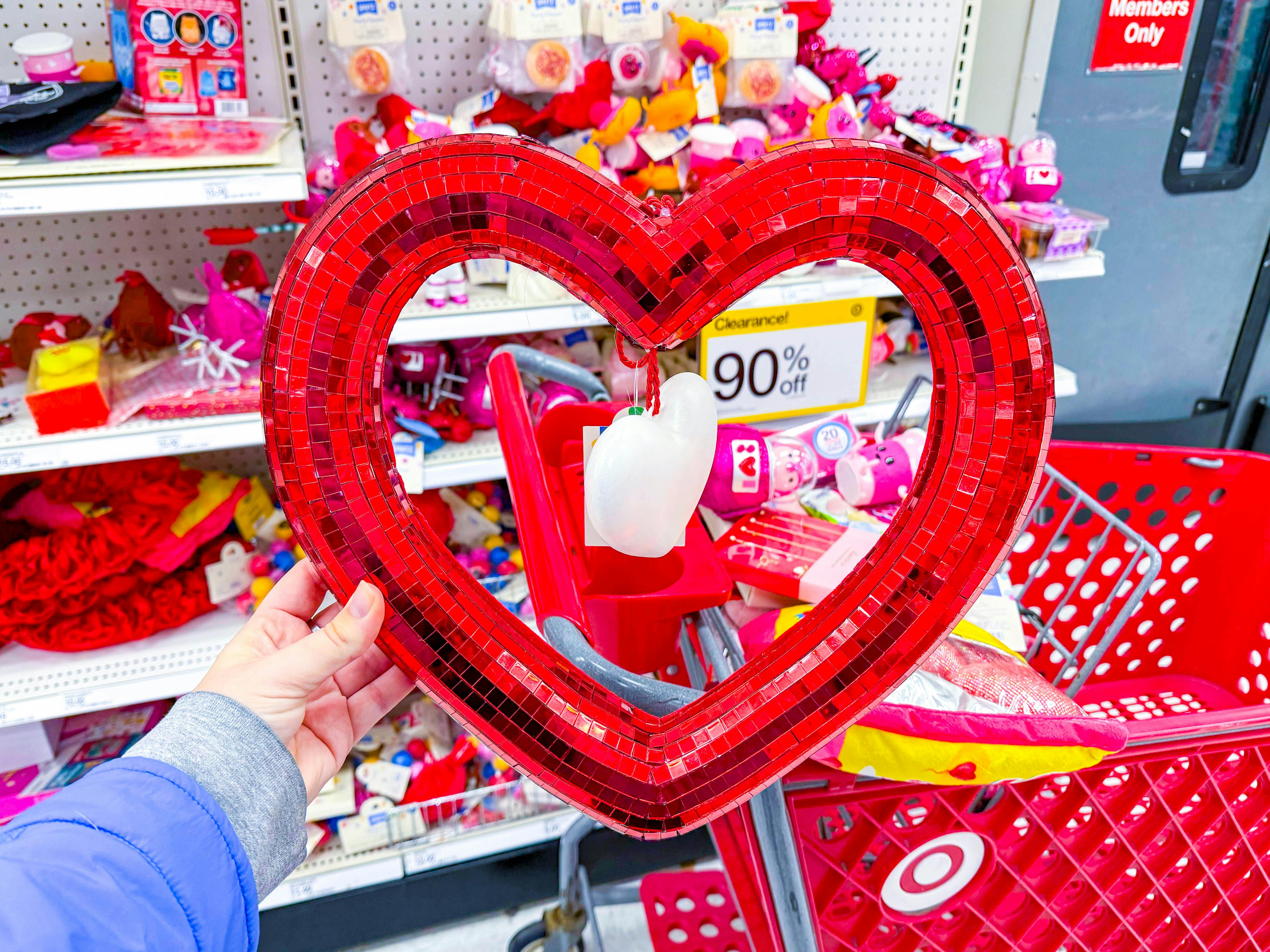 hand holding a red heart shaped wreath in front of a 90% off clearance signage at Target