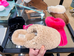 A hand picking up a pair of Ugg slippers