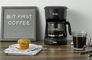 A coffee maker on a table with a muffin and cup of coffee