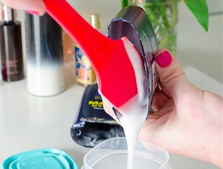 Someone scraping lotion into a small container.