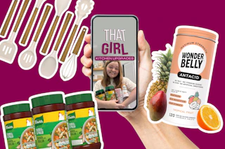 Hand holding phone with 'That Girl Kitchen Upgrades' video, surrounded by Knorr seasoning jars, Wonderbelly antacid, and fresh fruit