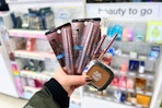 person holding maybelline and loreal makeup in front of the display