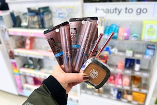 person holding maybelline and loreal makeup in front of the display