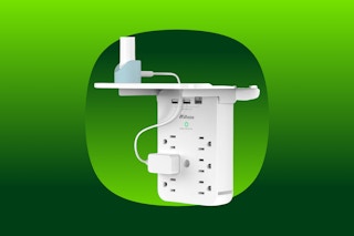 An outlet extender surge protector in white with a removable shelf on top that holds a charging tablet and phone