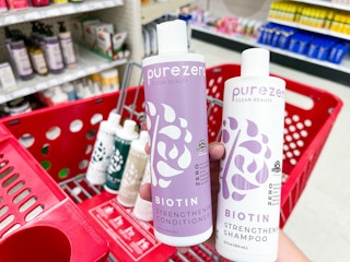 hand holding purezero shampoo & conditioner bottles over a target cart