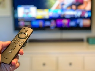 Amazon fire tv stick pointed at a tv with programs out of focus in the background.