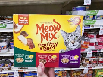 a hand holding a box of cat food cans in a store