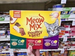 a hand holding a box of cat food cans in a store