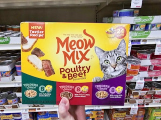 a hand holding a box of cat food cans in a store