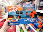 hand holding a nerf blaster in front of a target shelf