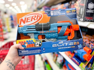hand holding a nerf blaster in front of a target shelf