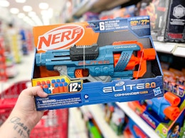 hand holding a nerf blaster in front of a target shelf