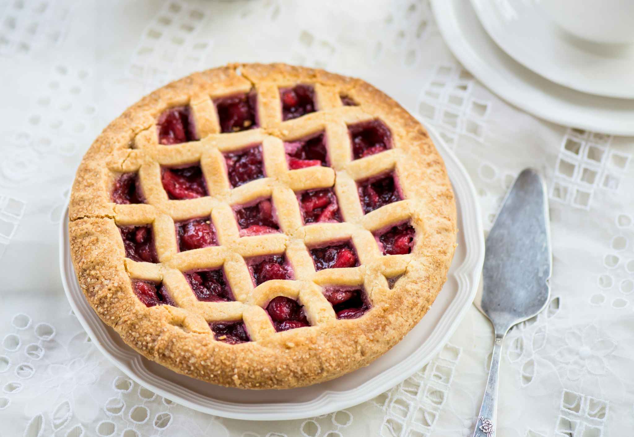 A pie with a no-weave lattice top crust sitting on a table next to a pie knife.