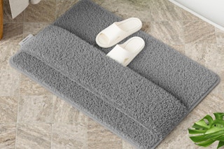 a grey bath mat with slippers on the floor in a bathroom