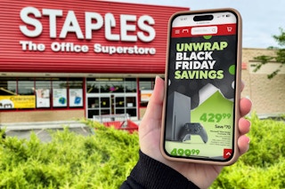 someone holding a phone showing the black friday ad in front of a staples store