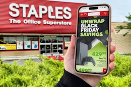 someone holding a phone showing the black friday ad in front of a staples store