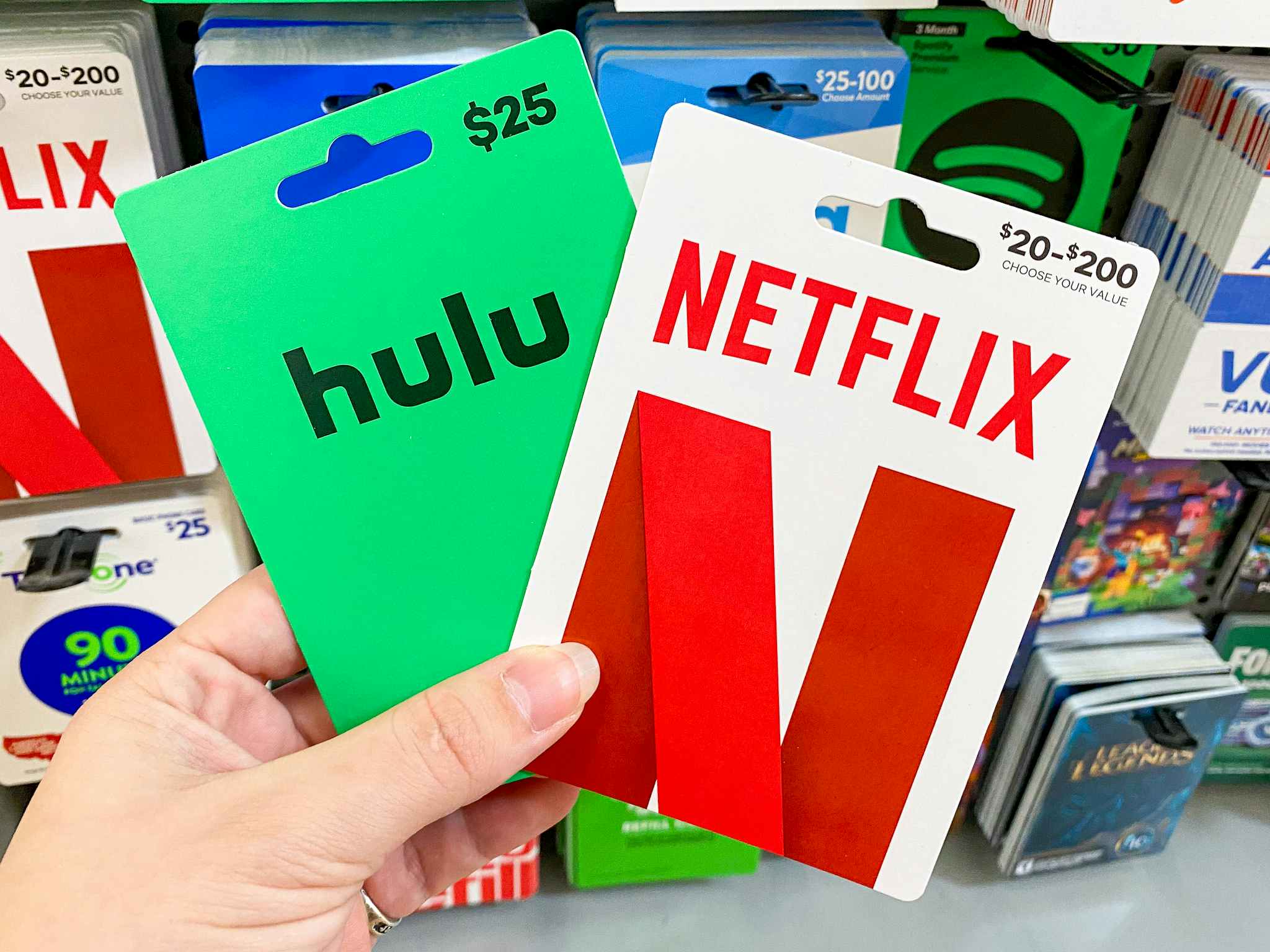 A person's hand holding Hulu and Netflix gift cards in front of a display of gift cards at Walmart.