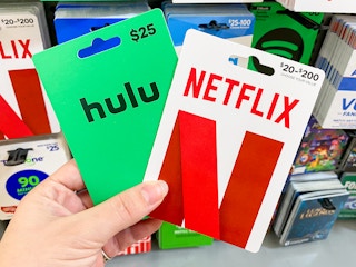 A person's hand holding Hulu and Netflix gift cards in front of a display of gift cards at Walmart.
