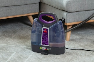 A Bissell carpet cleaner sitting on the floor next to a couch