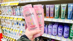 hand holding two l'oreal elvive glycolic gloss shampoos in walgreens