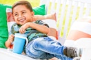 Lifestyle image of a small boy lounging while using the blue Munchkin Snack Catch and Sip