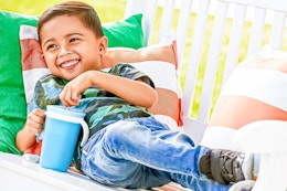 Lifestyle image of a small boy lounging while using the blue Munchkin Snack Catch and Sip