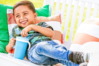 Lifestyle image of a small boy lounging while using the blue Munchkin Snack Catch and Sip