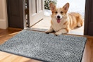 Corgi laying behind doormat in entrance