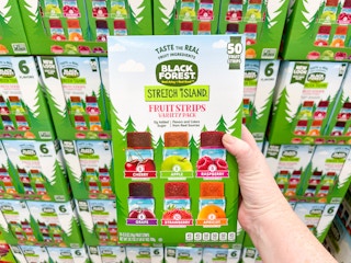 a hand holding a box of fruit snacks in front of other boxes