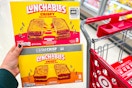 hand holding 2 boxes of lunchables grilled cheesies in front of a target cart