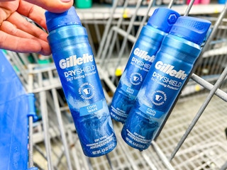 hand holding a blue bottle of Gillette Dry Spray in front of two other bottles in a Walmart cart