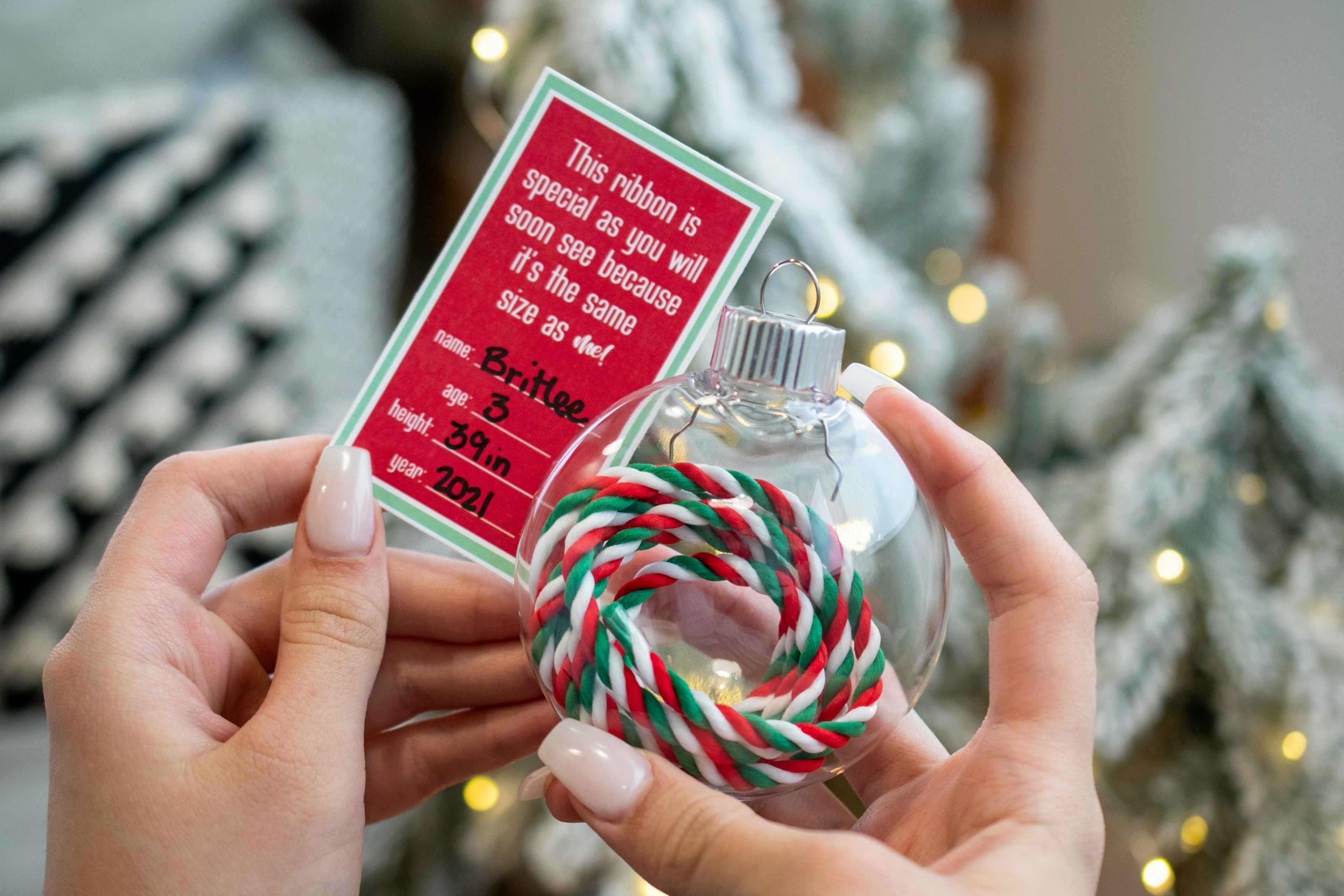 Someone holding a clear ornament with a ribbon inside it with a tag that says "This ribbon is special as you will soon see because it's t...