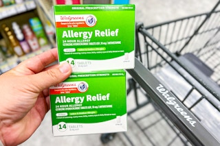 hand holding two boxes of allergy relief next to walgreens shopping cart