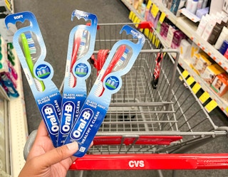 hand holding three Oral-B toothbrushes in front of shopping cart