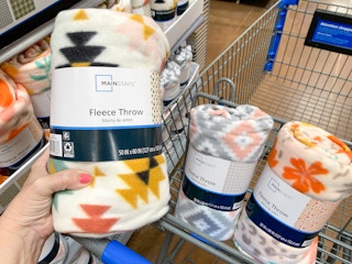 hand holding a mainstays fleece throw blanket with two in walmart cart