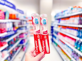 hand holding 2 colgate optic white toothbrushes in a target aisle