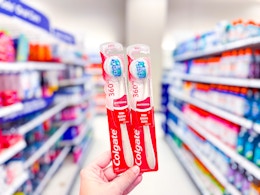 hand holding 2 colgate optic white toothbrushes in a target aisle