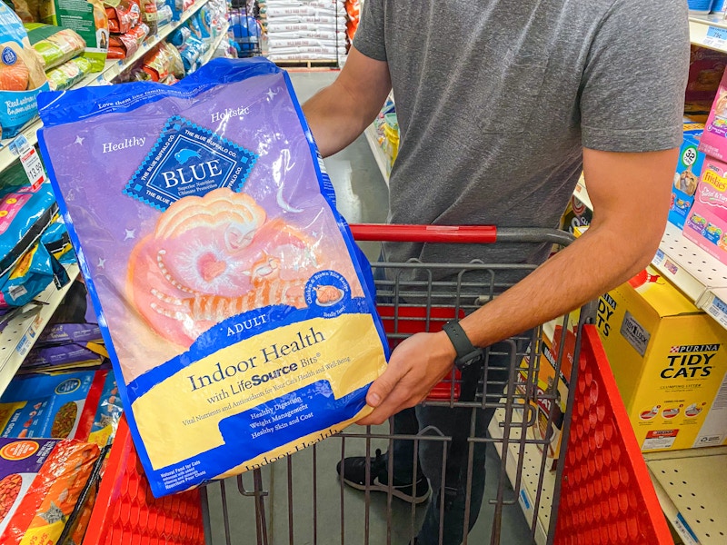 A man putting a bag of Blue Buffalo cat food into a Tractor Supply cart.