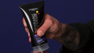 A hand squeezing a bottle of L'Oreal hair gel.