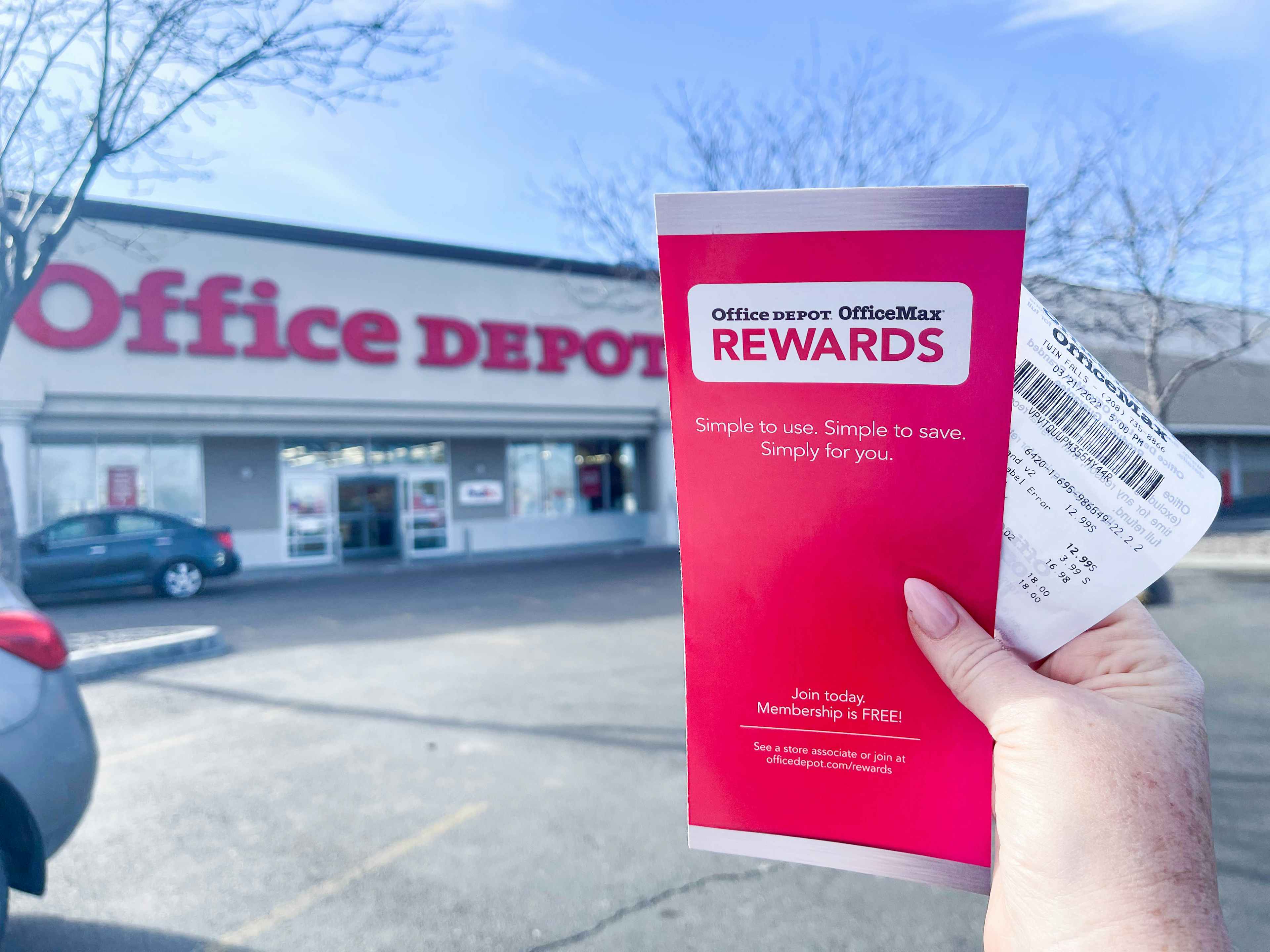 A person's hand holding up an Office Depot rewards brochure and a receipt outside of an Office Depot store.