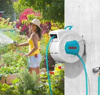 a garden hose reel on a wall outside while a woman is watering her garden