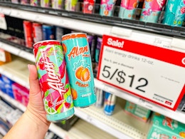 hand holding two cans of Alani Nu in front of the promotion