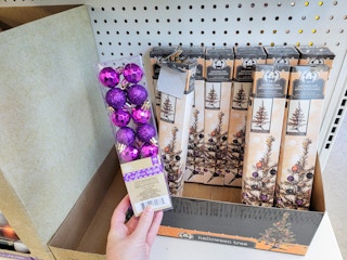 hand holding a pack of small purple ornaments in front of halloween trees